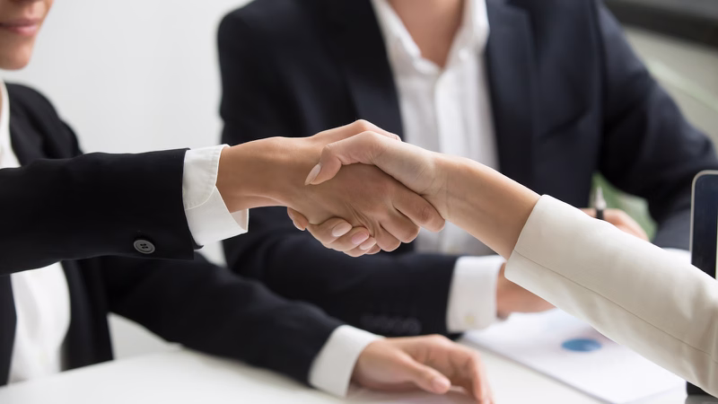 Zwei Personen geben sich am Schreibtisch die Hand – Sinnbild für die Übergabe an einen Nachfolger