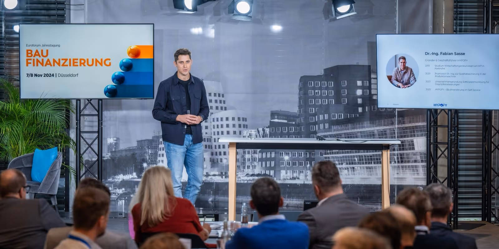 Dr. Fabian Sasse, der Gründer und CEO von HYPOFY auf der Bühne vor ca. 20 Zuschauern aus der Baufinanzierungs-Branche. Die Präsentation zeigt eine Folie mit der Überschrift: Baufinanzierung.