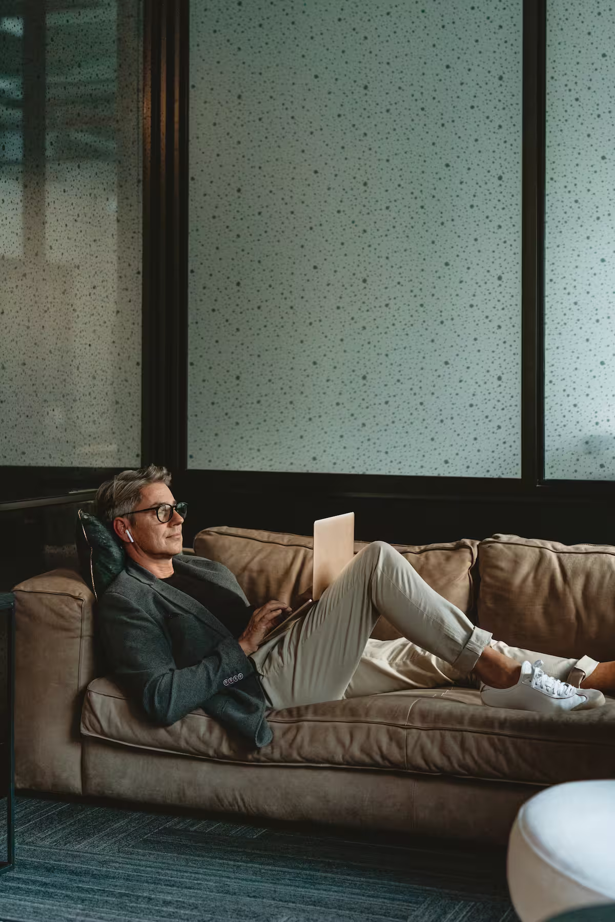 Atmosphärisches Bild eines Finanzberaters, der dank HYPOFY ganz entspannt auf einer Ledercouch seine Arbeit erledigen kann.